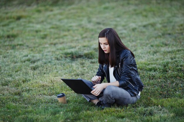 Young businesswoman sitting and working in park with laptop