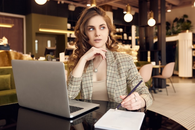 Young businesswoman in smart casual wear makes notes in a notebook in a coffee shop interior