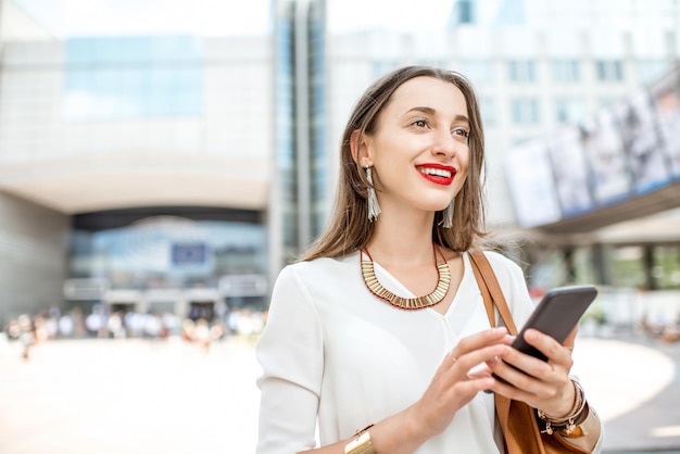 Young businesswoman standing with phone near the Parliament building of European Union in Brussel city