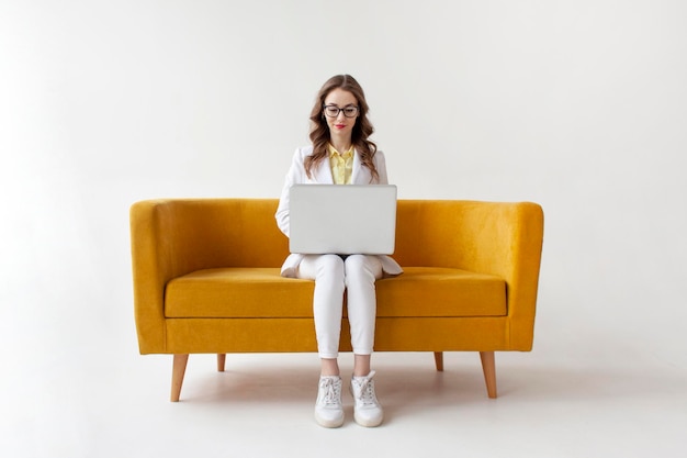 Young businesswoman in suit sits on comfortable soft sofa and uses laptop girl in formal wear