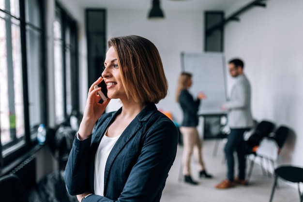 Young businesswoman talking on mobile phone with colleagues in background.