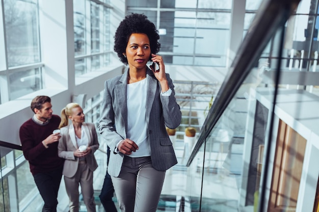 Young businesswoman talking on the phone while her coworkers drinking coffee behind her