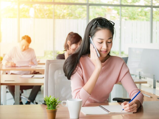 Photo young businesswoman talking on smartphone and using writing on notebook