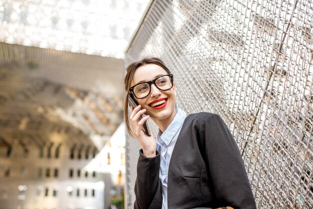 Young businesswoman talking with phone outdoors on the modern office district background