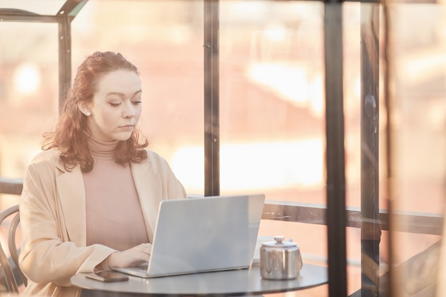 Young businesswoman typing on laptop computer and working online sitting at the table in coffee shop