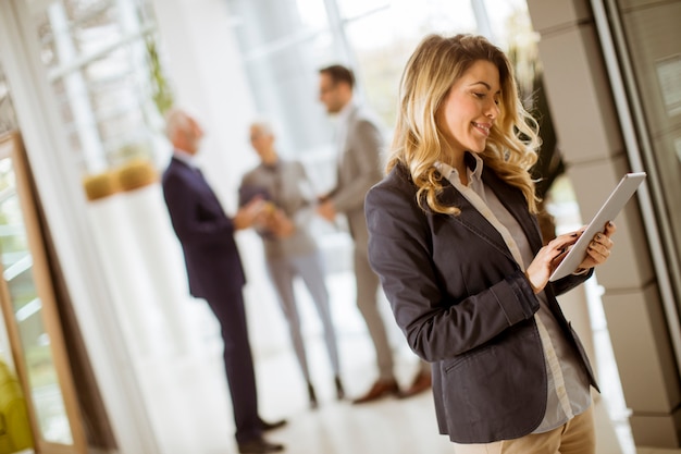 young businesswoman using with tablet in office while other business people talking in background