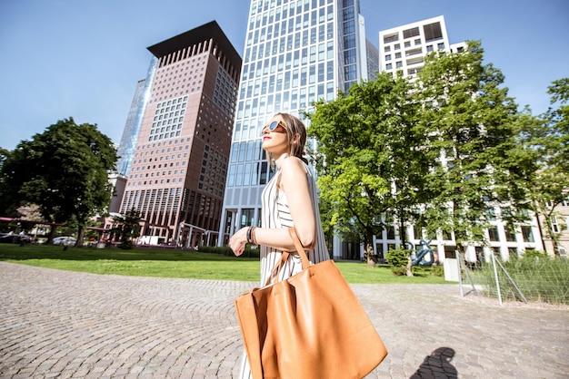 Young businesswoman walking outdoors at the modern district in Frankfurt city. View from below with skyscrapers on the background