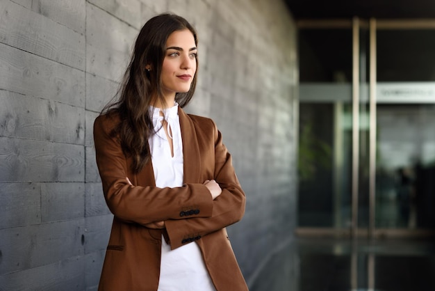 Young businesswoman with arms crossed standing against wall at office