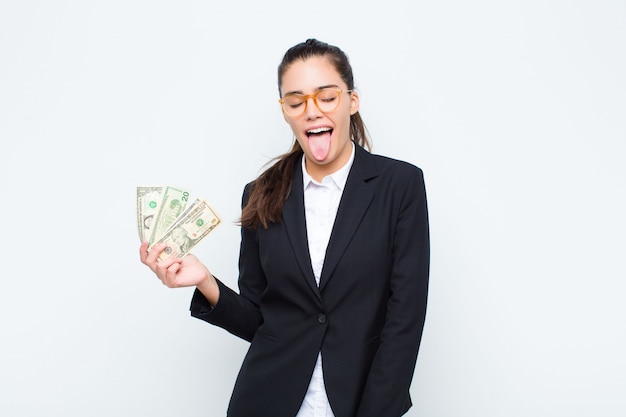 Young businesswoman with cheerful, carefree, rebellious attitude, joking and sticking tongue out, having fun with banknotes with bills