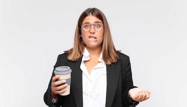 Young businesswoman with a coffee looking puzzled and confused, biting lip with a nervous gesture, not knowing the answer to the problem