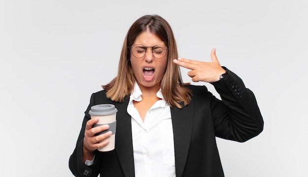 Foto giovane donna di affari con un caffè che sembra infelice e stressato, gesto di suicidio che fa il segno della pistola con la mano, indicando la testa