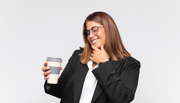 Young businesswoman with a coffee smiling with a happy, confident expression with hand on chin, wondering and looking to the side