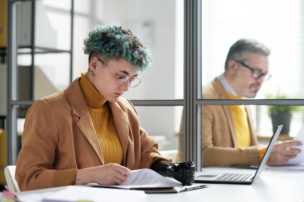 職場でラップトップを持って座ってオフィスで書類を処理している障害のある若いビジネスウーマン