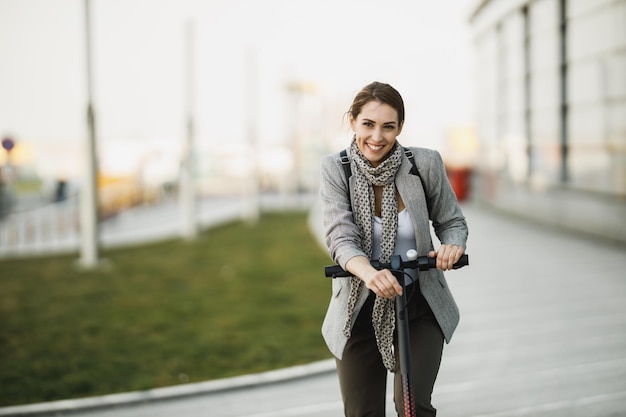 Una giovane donna d'affari con uno scooter elettrico a spinta che va al lavoro per la città.