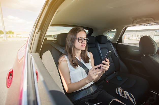 Young businesswoman with gadget sitting in modern car