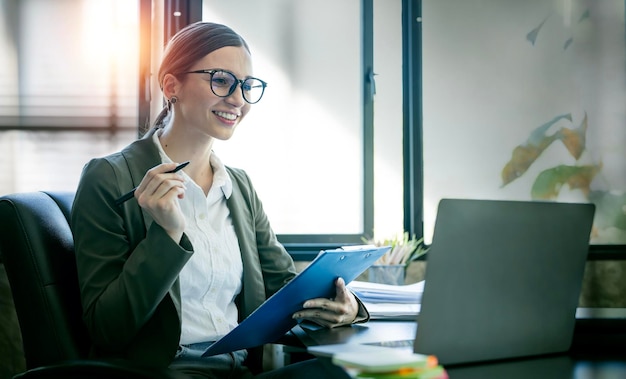 Young businesswoman with glasses working on document and laptop computer at office