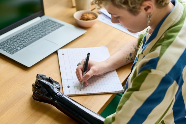 Young businesswoman with partial arm making notes or writing down plan