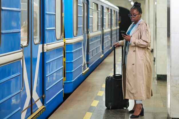 Young businesswoman with suitcase standing on platform in front of blue moving train