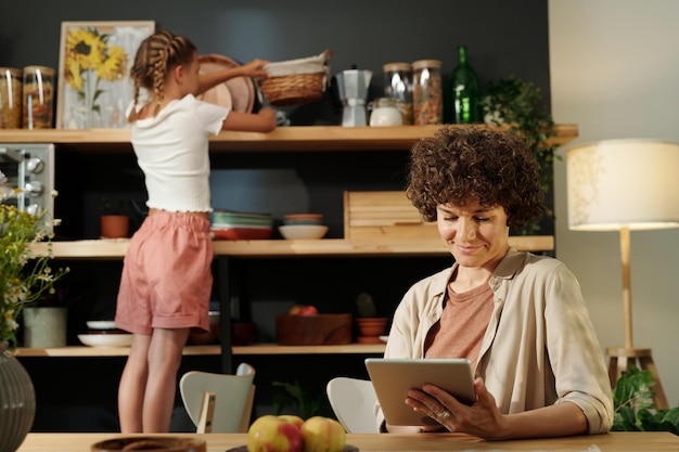 Young businesswoman with tablet networking by table against her daughter