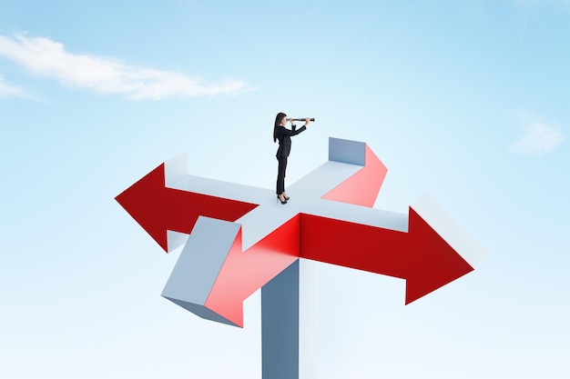 Young businesswoman with telescope standing on abstract arrow sign and looking into bright blue sky different direction choice and success concept