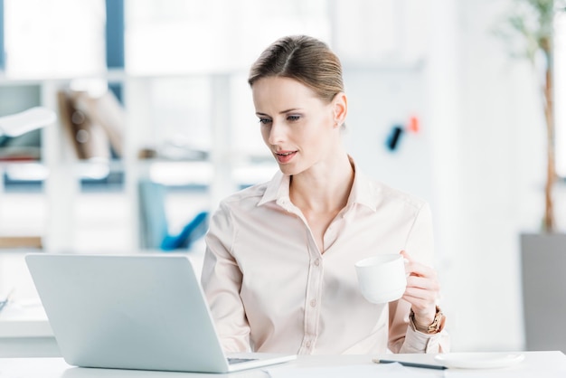 Young businesswoman working on laptop and drinking coffee at office