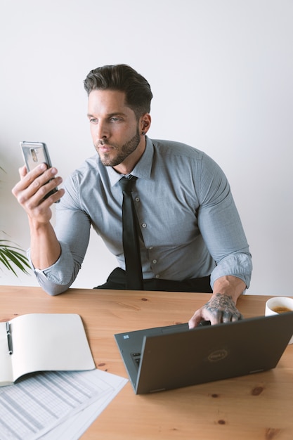 Young bussinesman working on laptop while he checks phone