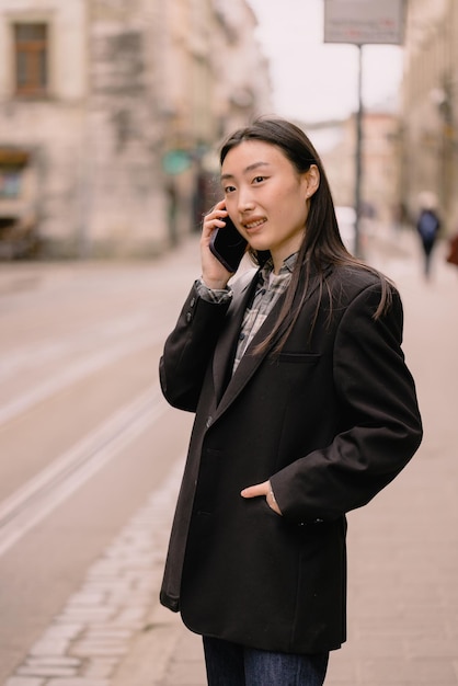young busy successful beautiful asian business woman korean professional businesswoman holding cellphone using smartphone standing or walking on old city street outside