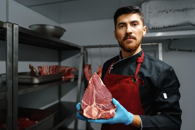 Фото Молодой мясник держит стейки из сырого мяса в холодильнике продуктового магазина