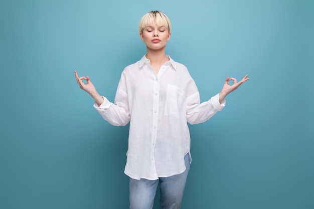 Young calm pretty blonde businesswoman in a white shirt is meditating on the background with copy