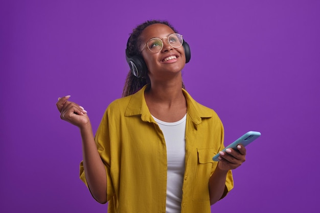 Young carefree african american woman with phone listens to music in headphones