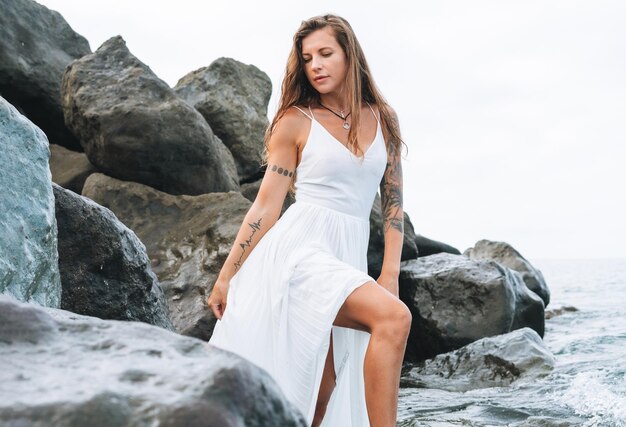 Young carefree beautiful woman with long hair in white dress enjoying life on sea beach