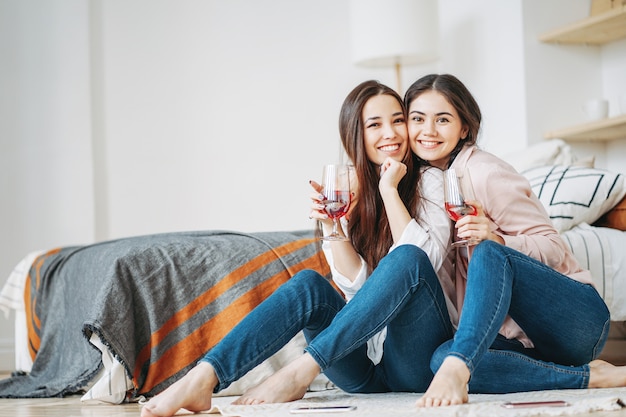 Foto giovani amici di ragazze spensierate del brunette in casuale con i bicchieri di vino divertendosi insieme sulla festa a casa