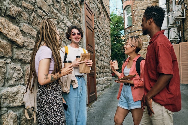 Young carefree friends with drinks standing by modern building