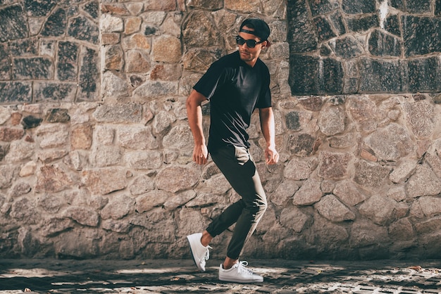 Young and carefree. Full length of handsome young African man in casual clothes moving and gesturing while standing against the stoned wall outdoors