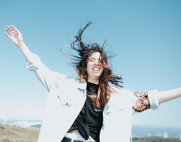 写真 流行のモダンな服を着た若い屈託のない女性が、風が髪を動かしながら祝うのを楽しんでいます お祝いと休日のコンセプト 若者の自由の自由 新しい生活 新しい日 新しい機会