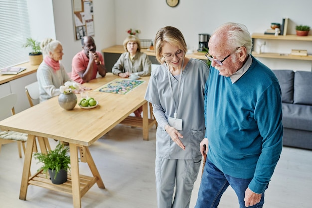 Young caregiver helping senior man to walk she caring about senior people in nursing home