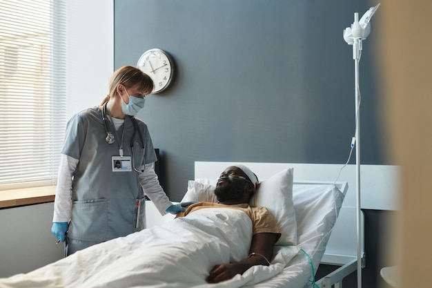 Young caregiver in protective mask communicating with injured patient