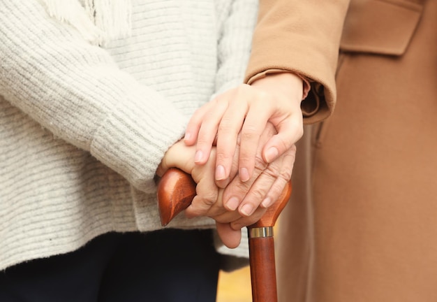 Young caregiver supporting senior woman with cane closeup