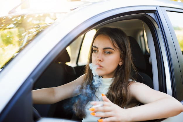 Young careless girl driving parents` car and smoking. Arrogant woman in bad mood driving car