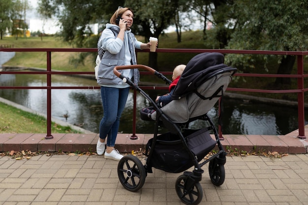 写真 生まれたばかりの子供と一緒にベビーカーの横にコーヒーを片手に思いやりのある若い母親