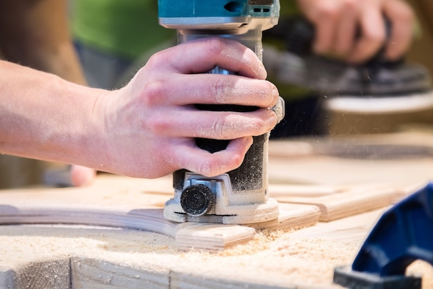 Young carpenter grinding cut out wood decoration with electric sandpaper machine