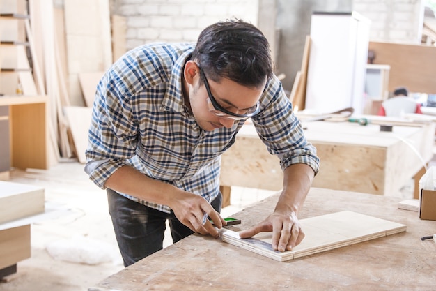 Young carpenter measuring and marking the wood board