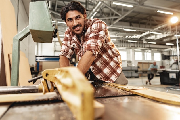 Foto giovane falegname che lavora su macchine per la lavorazione del legno nella fabbrica di mobili da vicino