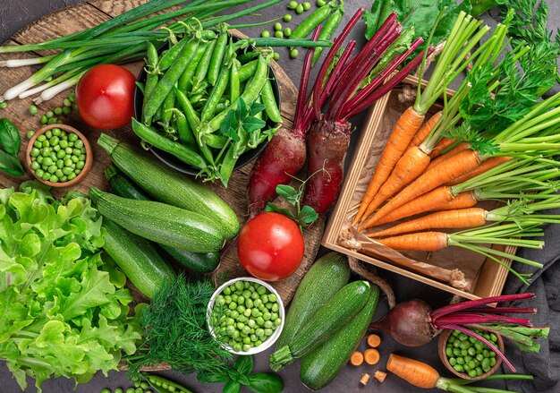 Young carrots, zucchini, tomatoes, peas and greens on a brown background. Top view, close-up.