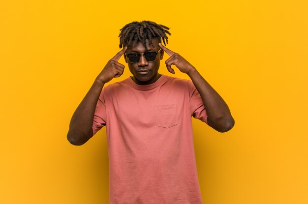 Young casual black man wearing sunglasses focused on a task, keeping him forefingers pointing head.