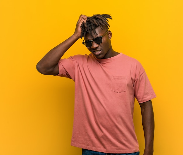 Young casual black man wearing sunglasses tired and very sleepy keeping hand on his head.