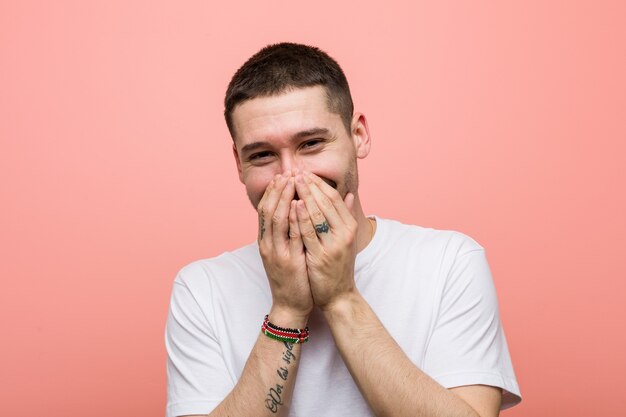 Young casual man laughing about something, covering mouth with hands.