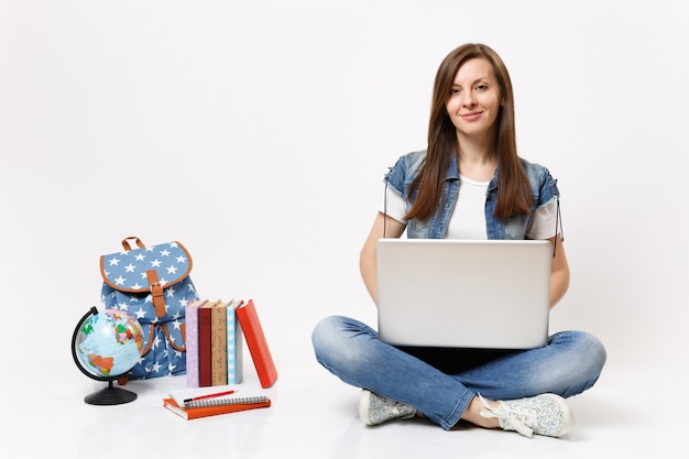 Young casual pretty smiling woman student holding using laptop pc computer sitting near globe, backpack, school books