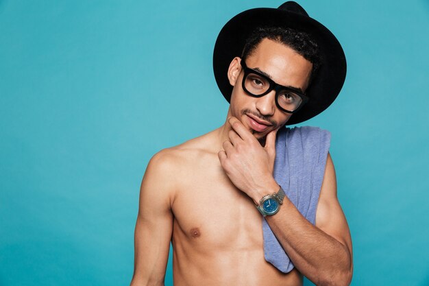 Young casual shirtless african man in hat and eyeglasses thinking