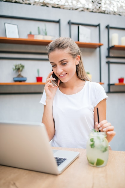 Young casual woman drinking lemonade and talking over mobile phone.